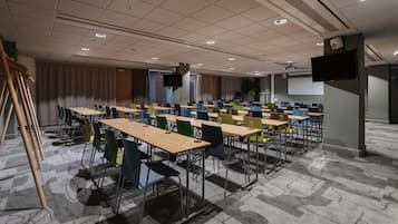 Un salón de conferencias con varias mesas y sillas, una pantalla de proyector y un televisor.