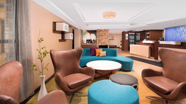 A hotel lobby with leather armchairs, a blue sofa, a white coffee table, and a stone fireplace. - Fairfield Inn & Suites Albany East Greenbush (East Greenbush)