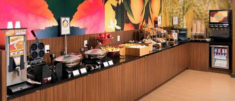 Un espace buffet proposant une variété de plats, une machine à café et un écran de télévision affichant un menu.