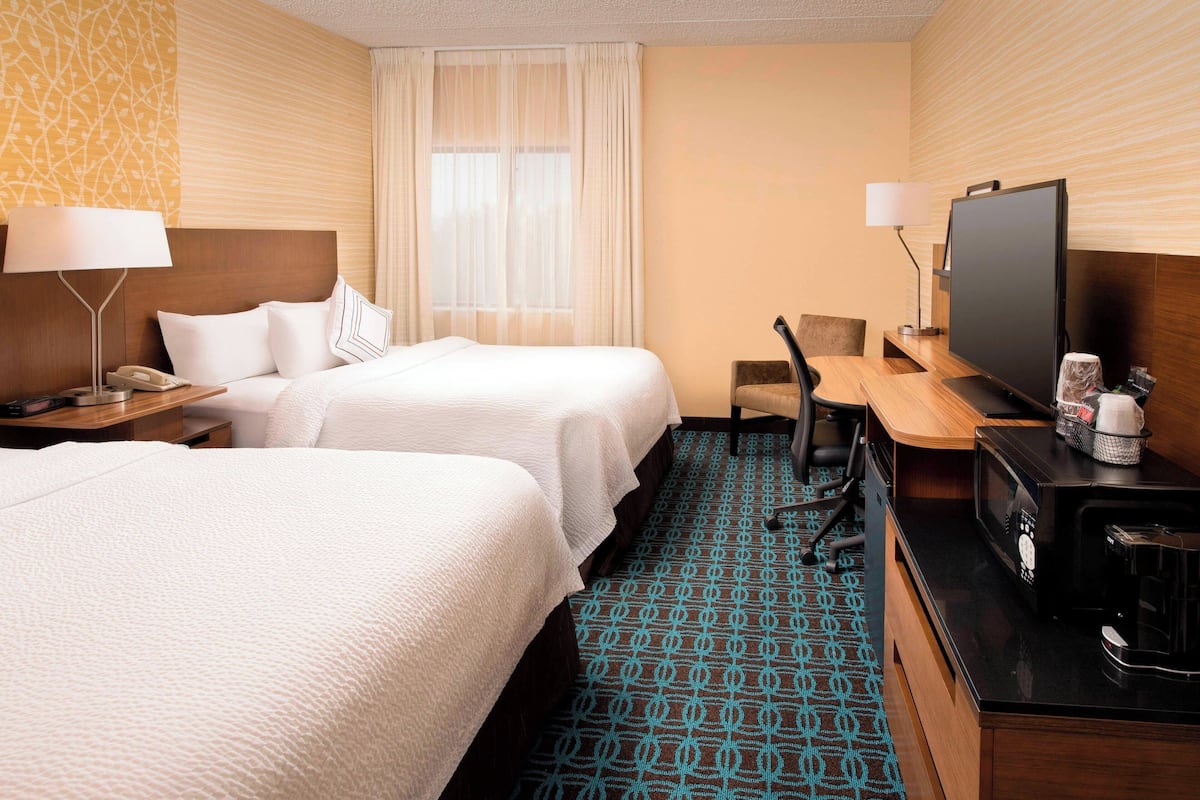 Une chambre d’hôtel avec deux lits, un bureau avec une télévision, une machine à café et une chaise.