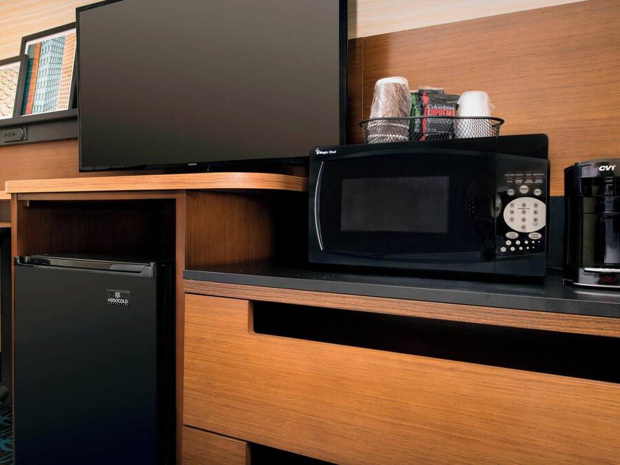 Een kitchenette met een koelkast, magnetron en koffiezetapparaat.