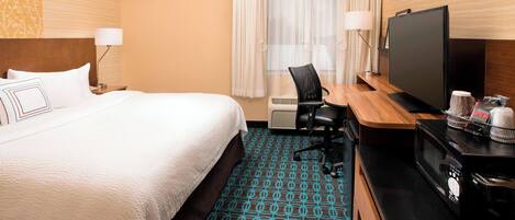 A hotel room with a bed, a desk with a TV, a microwave, and a coffee maker.