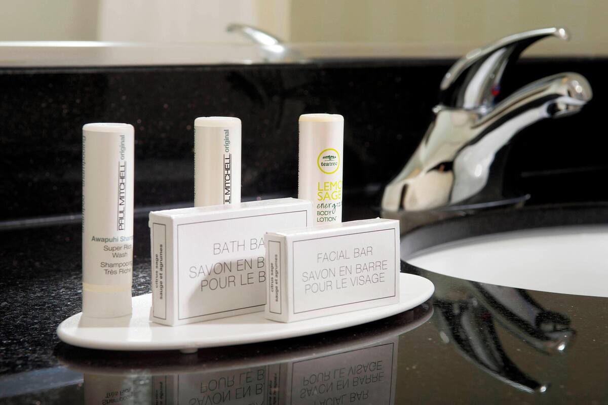 A bathroom counter with three toiletries: a shampoo bottle, a body lotion, and a facial bar.