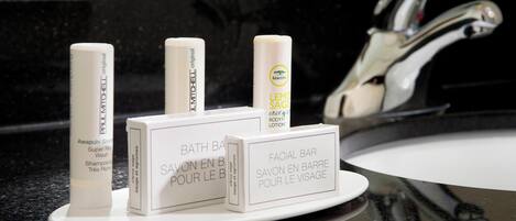 Una encimera de baño con tres artículos de tocador: una botella de champú, una loción corporal y una pastilla facial.