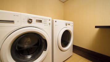 Two front-loading washing machines in a laundry room with wooden flooring and a dark-colored wall.