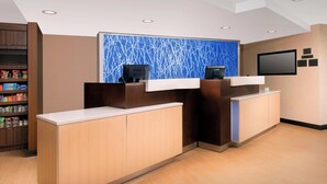 A hotel reception area with a modern design, featuring a reception desk, a wall-mounted TV, and a shelf with snacks. - Fairfield Inn & Suites Albany East Greenbush (East Greenbush)