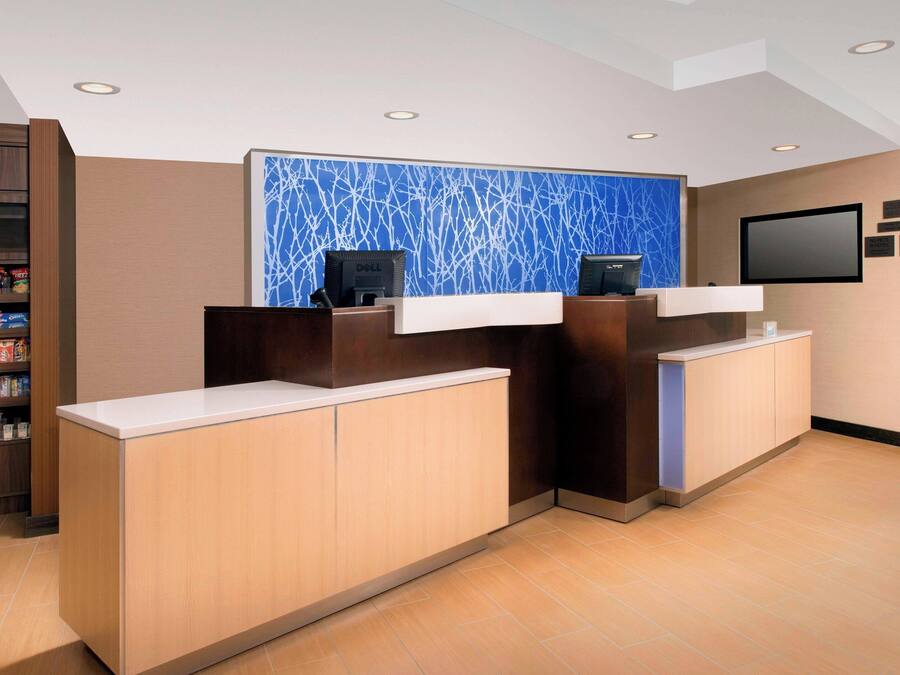 A hotel reception area with a modern design, featuring a reception desk, a wall-mounted TV, and a shelf with snacks.