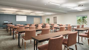 Un salón de conferencias con varias mesas y sillas, una pantalla de proyector y un ventanal grande.