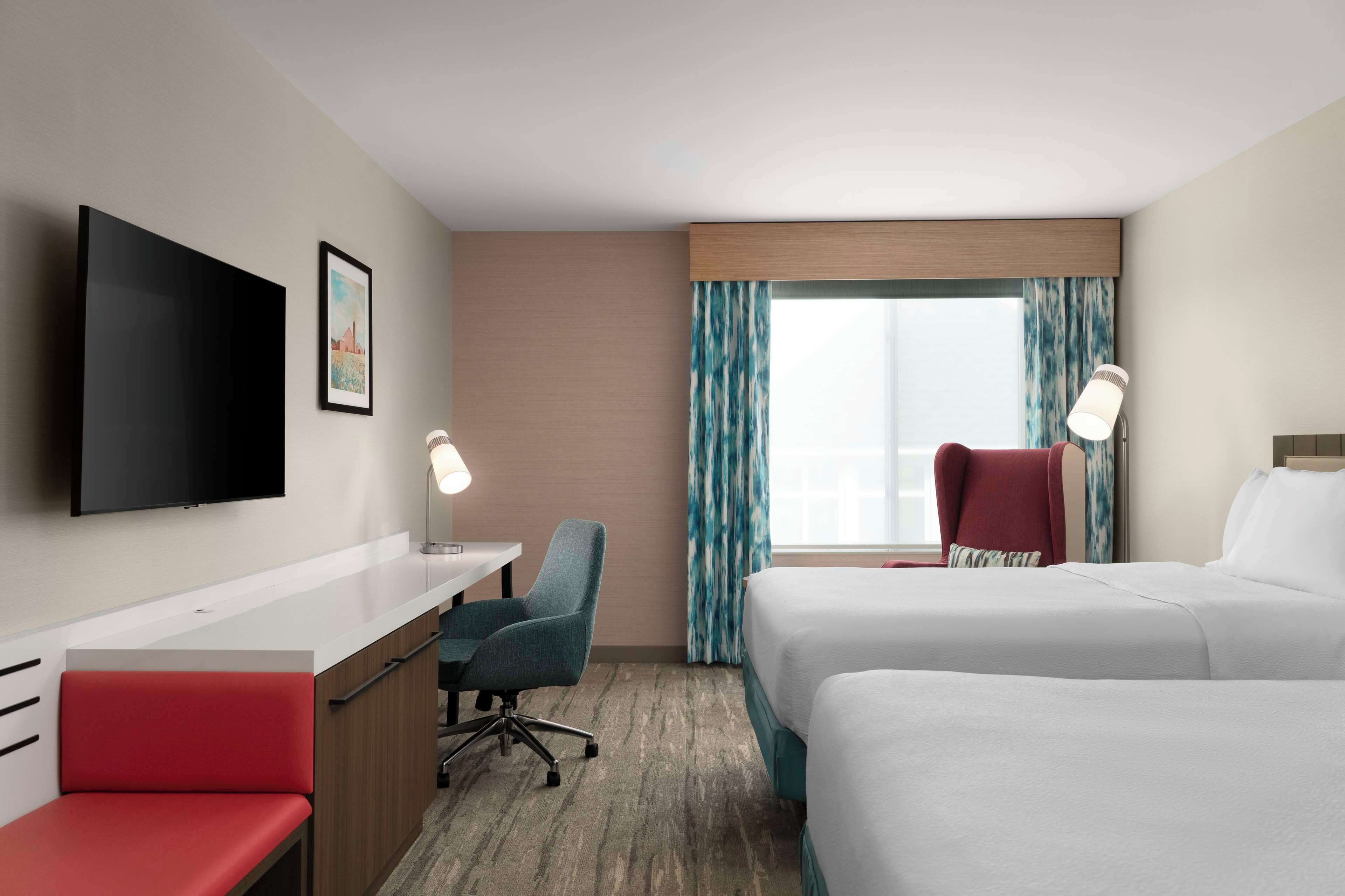 A hotel room with a bed, a desk, a chair, a TV, and a window with curtains.