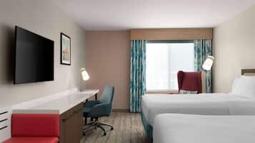 A hotel room with a bed, a desk, a chair, a TV, and a window with curtains.