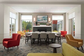 A modern dining area with a fireplace, large windows, and a mix of red and yellow chairs. - Hilton Garden Inn Kennett Square (Kennett Square)