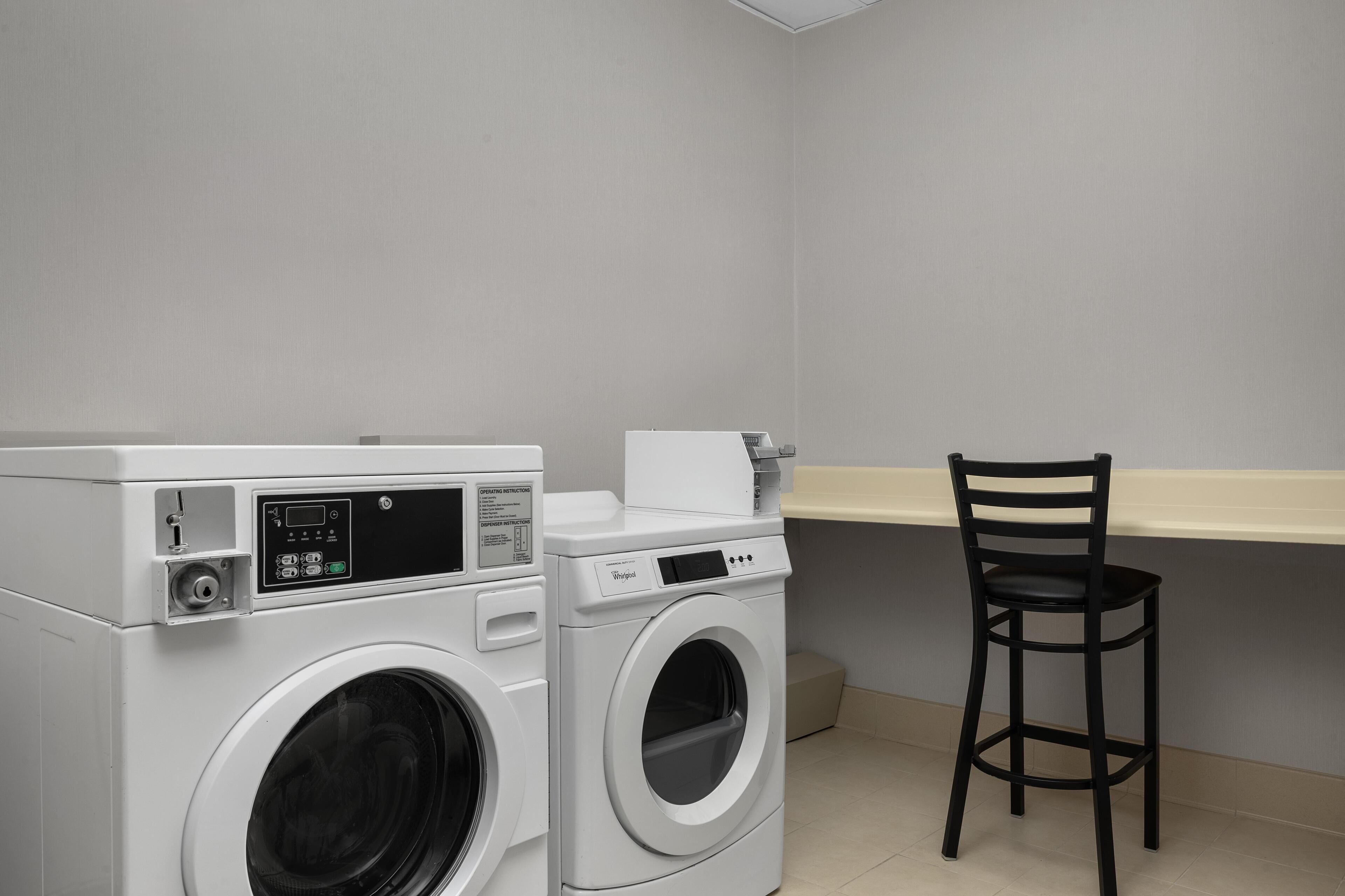 Un área de lavandería con lavadora, secadora y una silla.