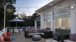 An outdoor patio with wicker furniture, a round table, and string lights. - Hilton Garden Inn Hilton Head (Hilton Head Island)