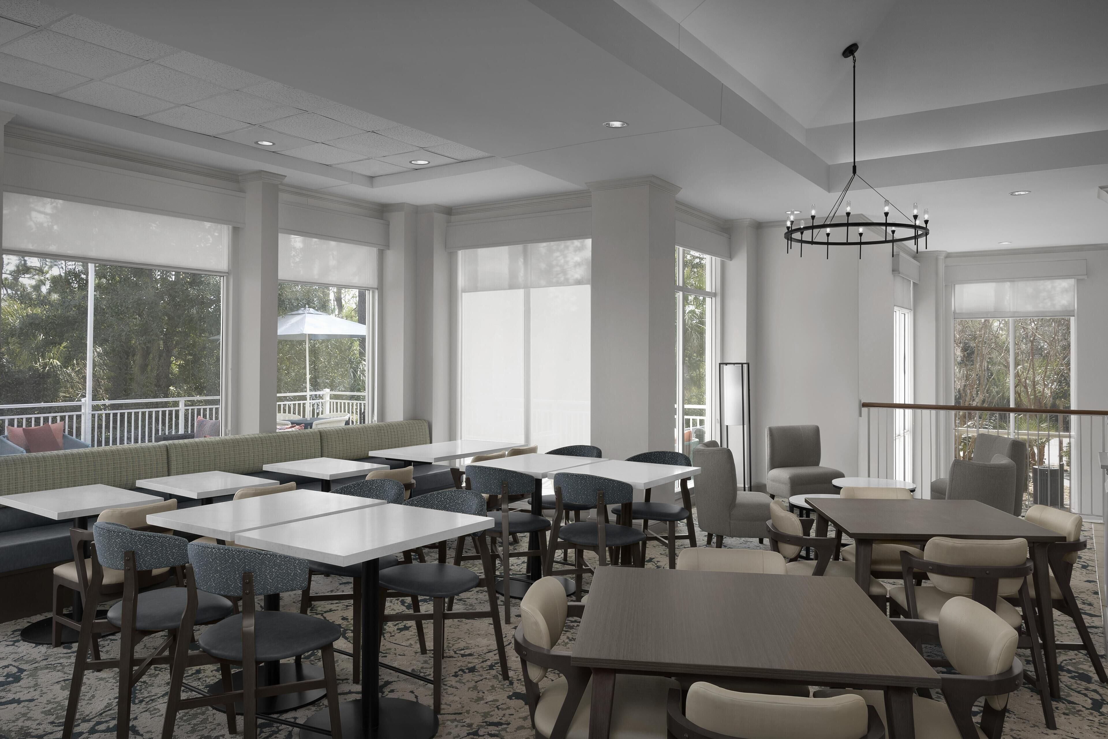 Un vaste espace dédié à la salle à manger, avec de nombreuses tables et chaises, de grandes fenêtres et un luminaire au plafond.
