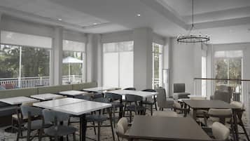A spacious dining area with multiple tables and chairs, large windows, and a ceiling light fixture.