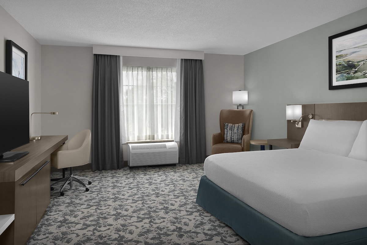 A hotel room with a bed, desk, chair, and a window with curtains.