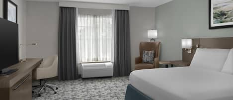 A hotel room with a bed, desk, chair, and a window with curtains.