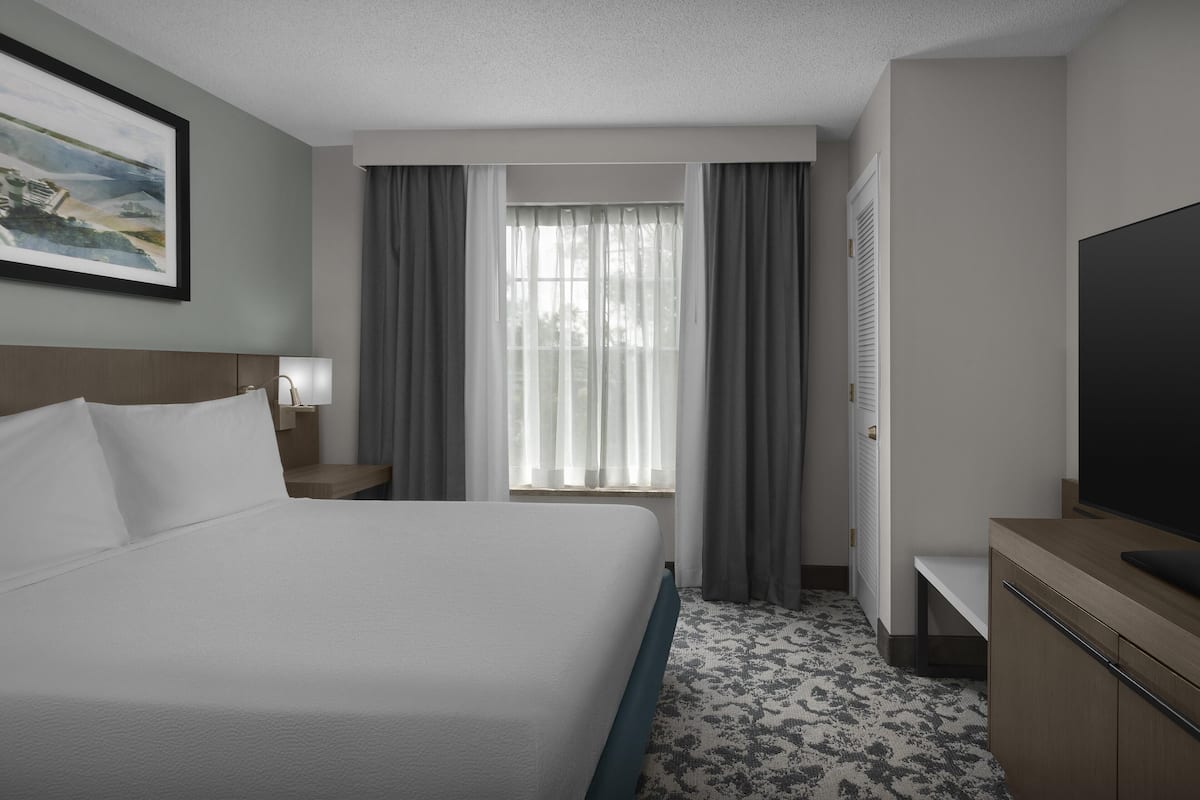 A hotel room with a bed, a television, a desk, and a window with curtains.