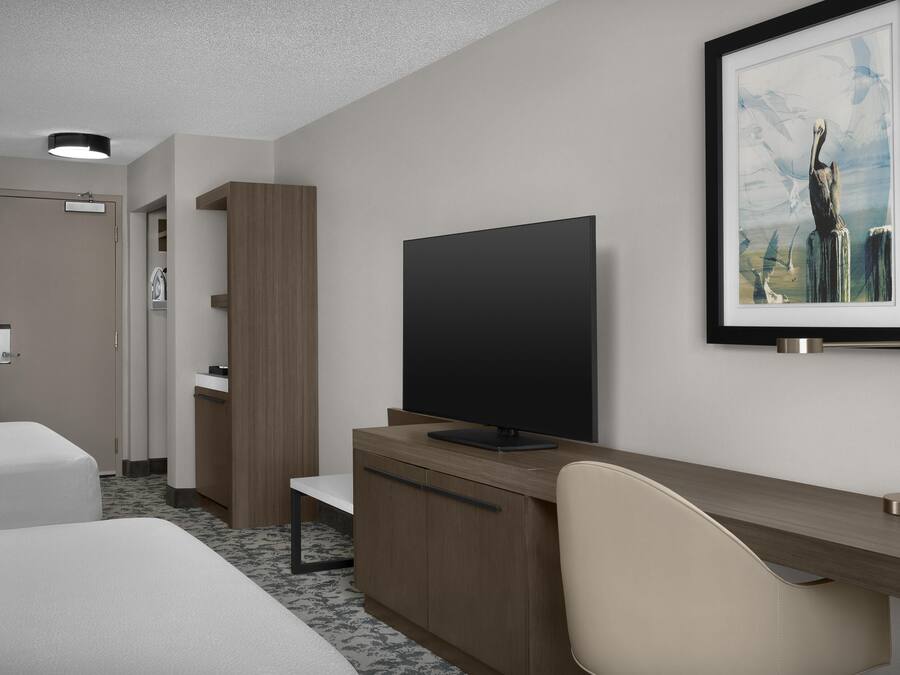 Une chambre d’hôtel avec un lit, un bureau avec un ordinateur, une chaise, une télévision et un tableau encadré au mur.