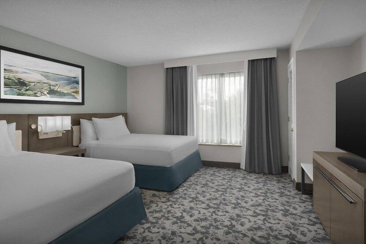 A hotel room with two beds, a TV, a desk, and a painting on the wall.