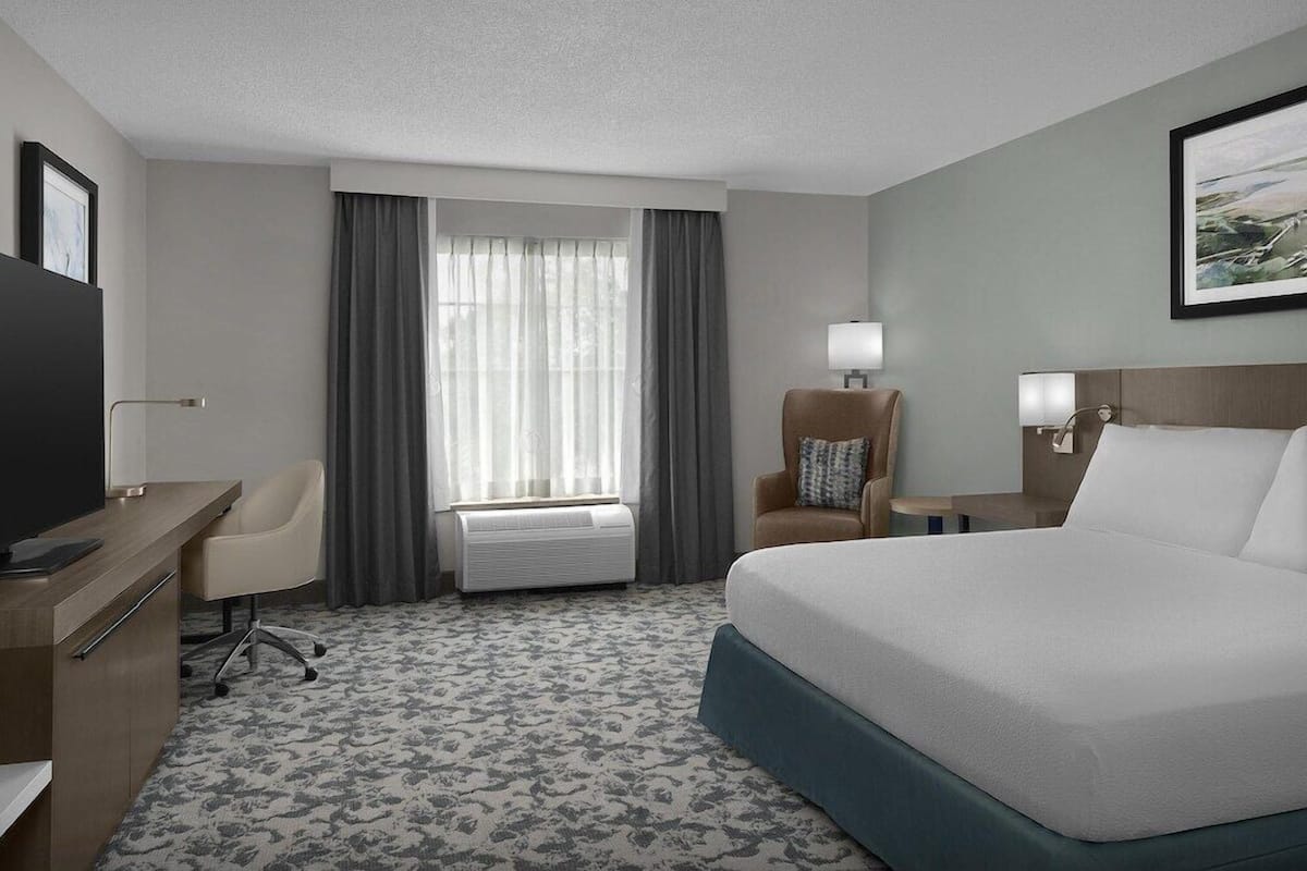 A hotel room with a bed, desk, chair, and a window with curtains.