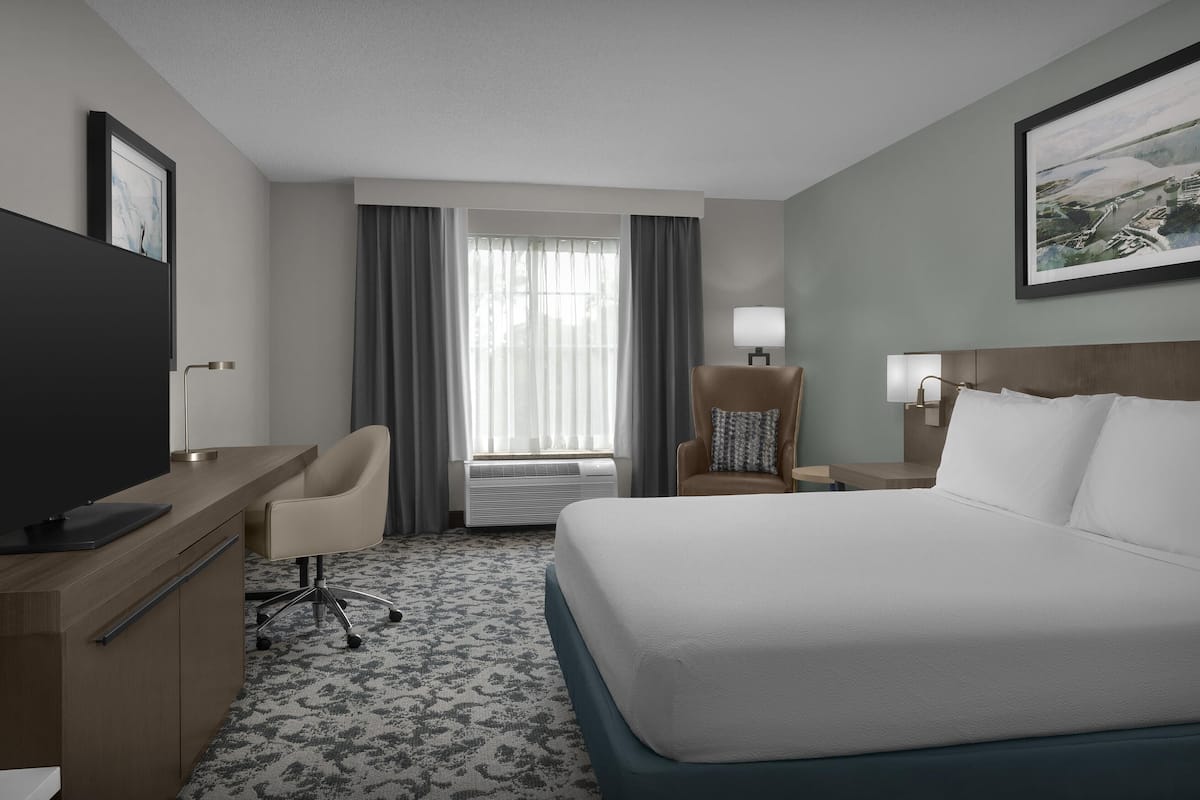 A hotel room with a bed, desk, chair, TV, and a window with curtains.