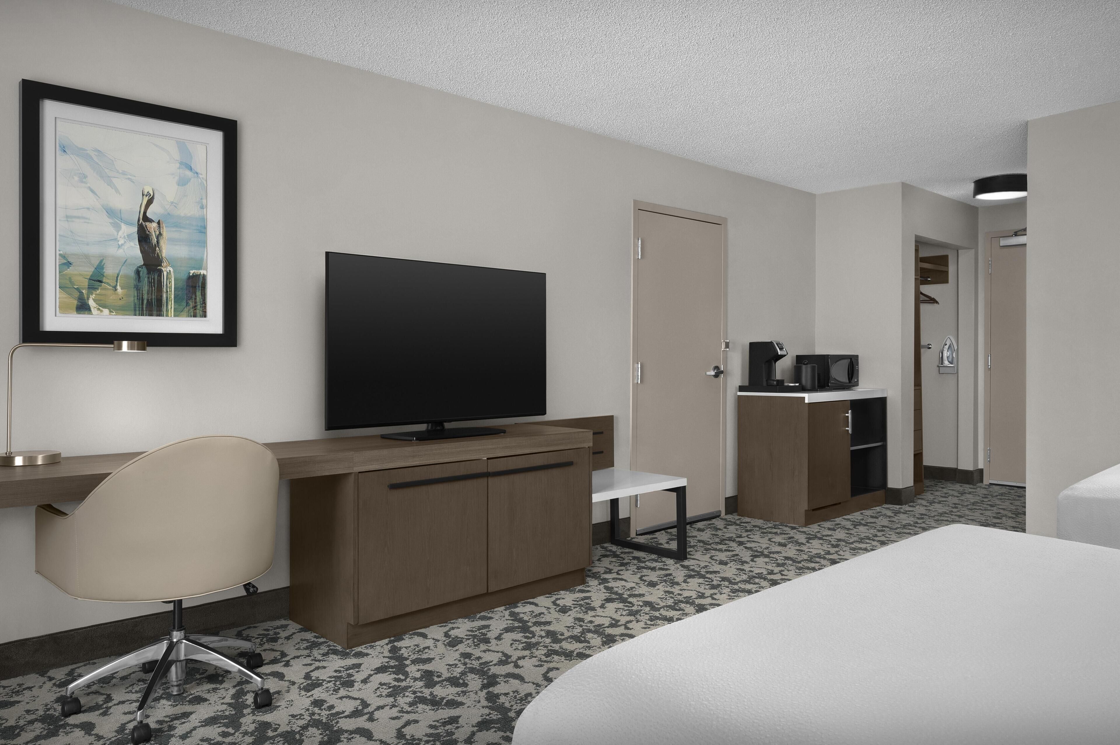 Une chambre d’hôtel équipée d’un lit, d’un bureau, d’une chaise, d’une télévision et d’un tableau encadré au mur.