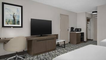 A hotel room with a bed, desk, chair, television, and a framed picture on the wall.