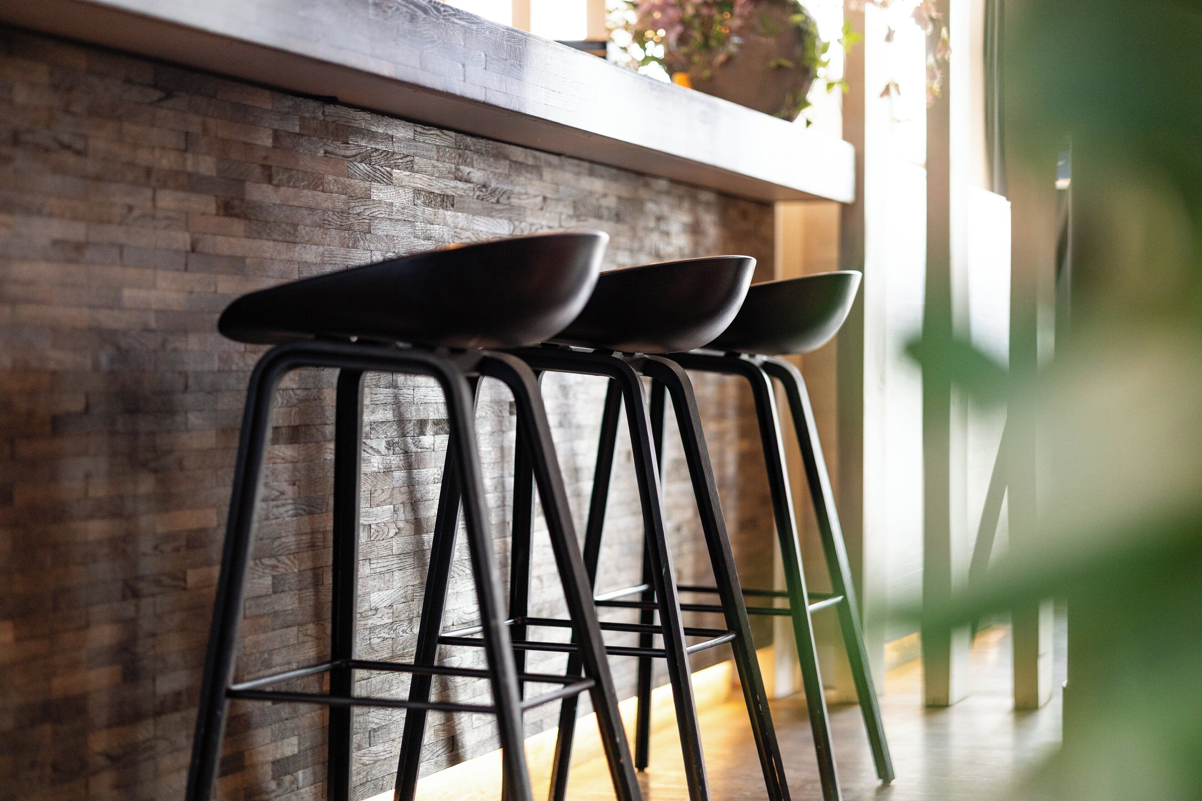 A row of black bar stools against a brick wall with a wooden countertop above.