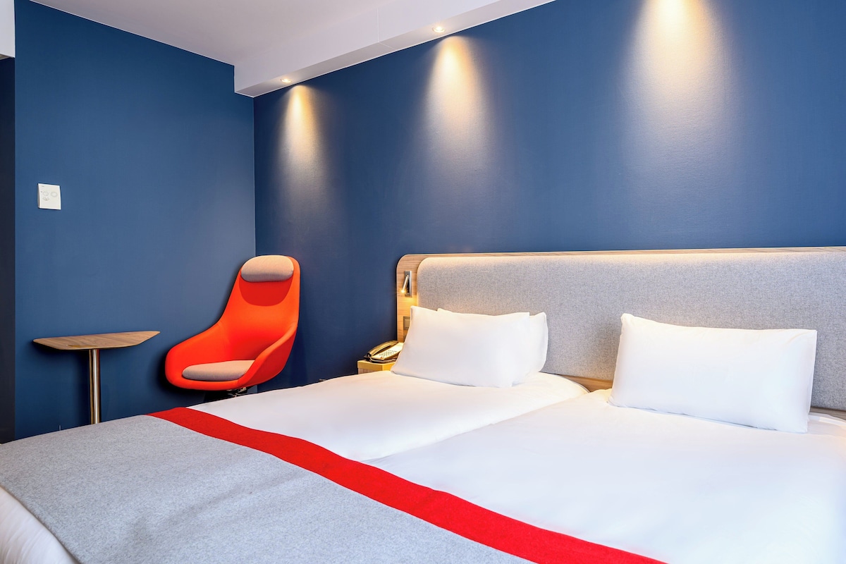 A hotel room with a large bed, a red chair, and a small table.