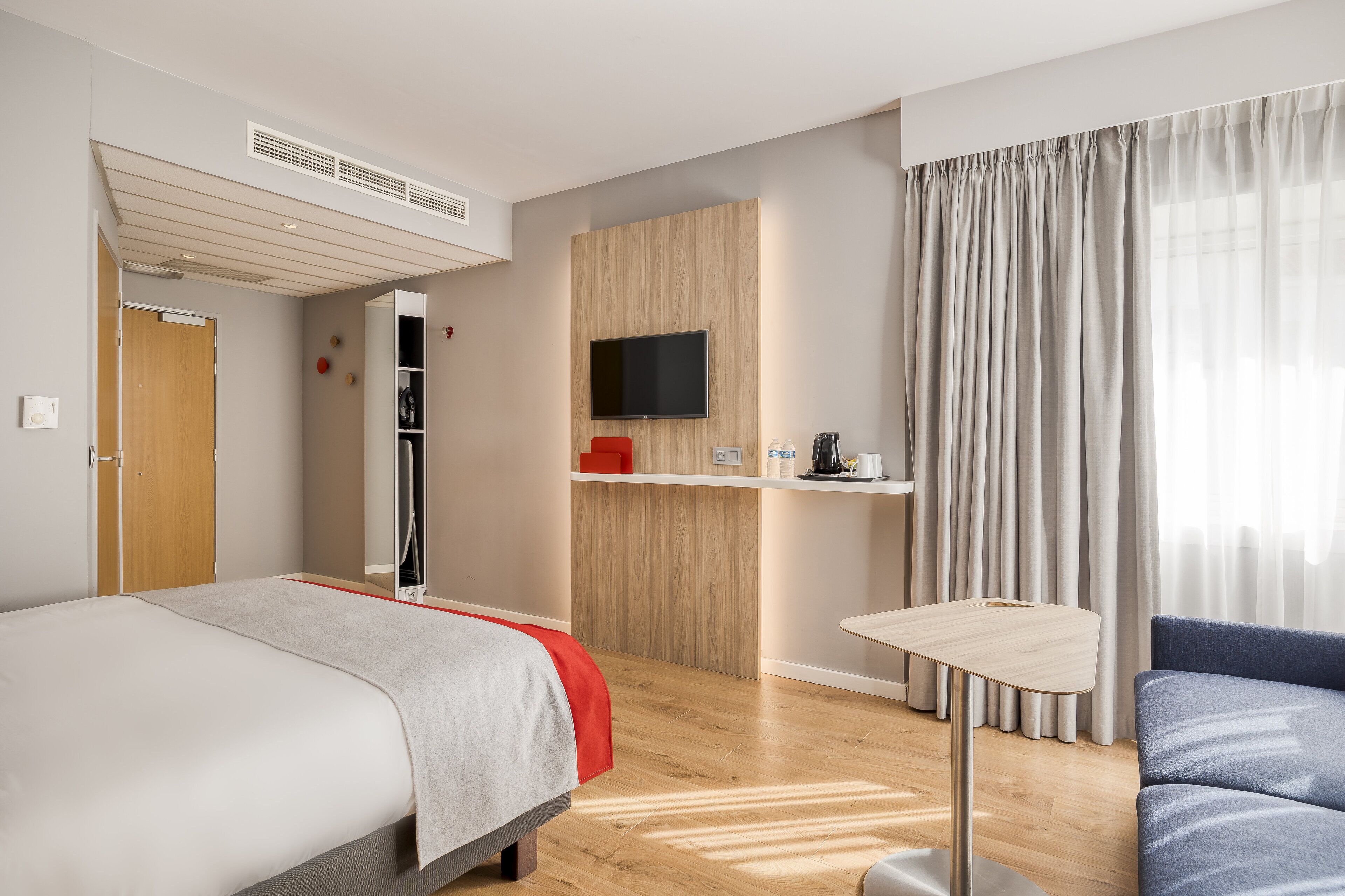 A modern hotel room with a bed, a desk, a TV, and a sofa.