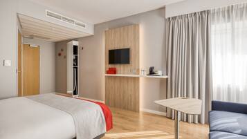 Quarto de hotel moderno com cama, escrivaninha, televisão e sofá.