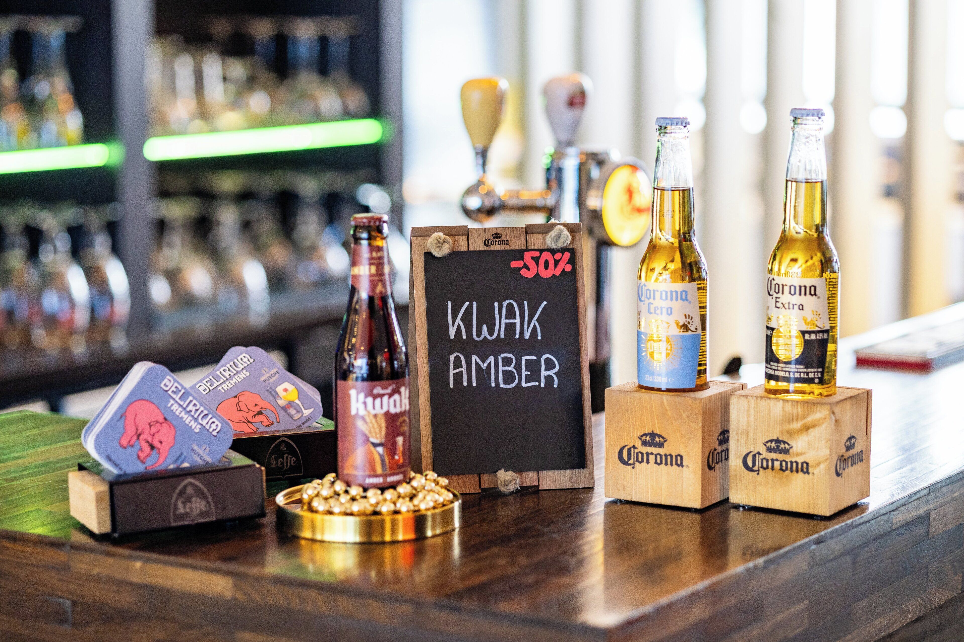 Una barra con varias botellas de cerveza, un cartel de pizarra y una bandeja de aperitivos.