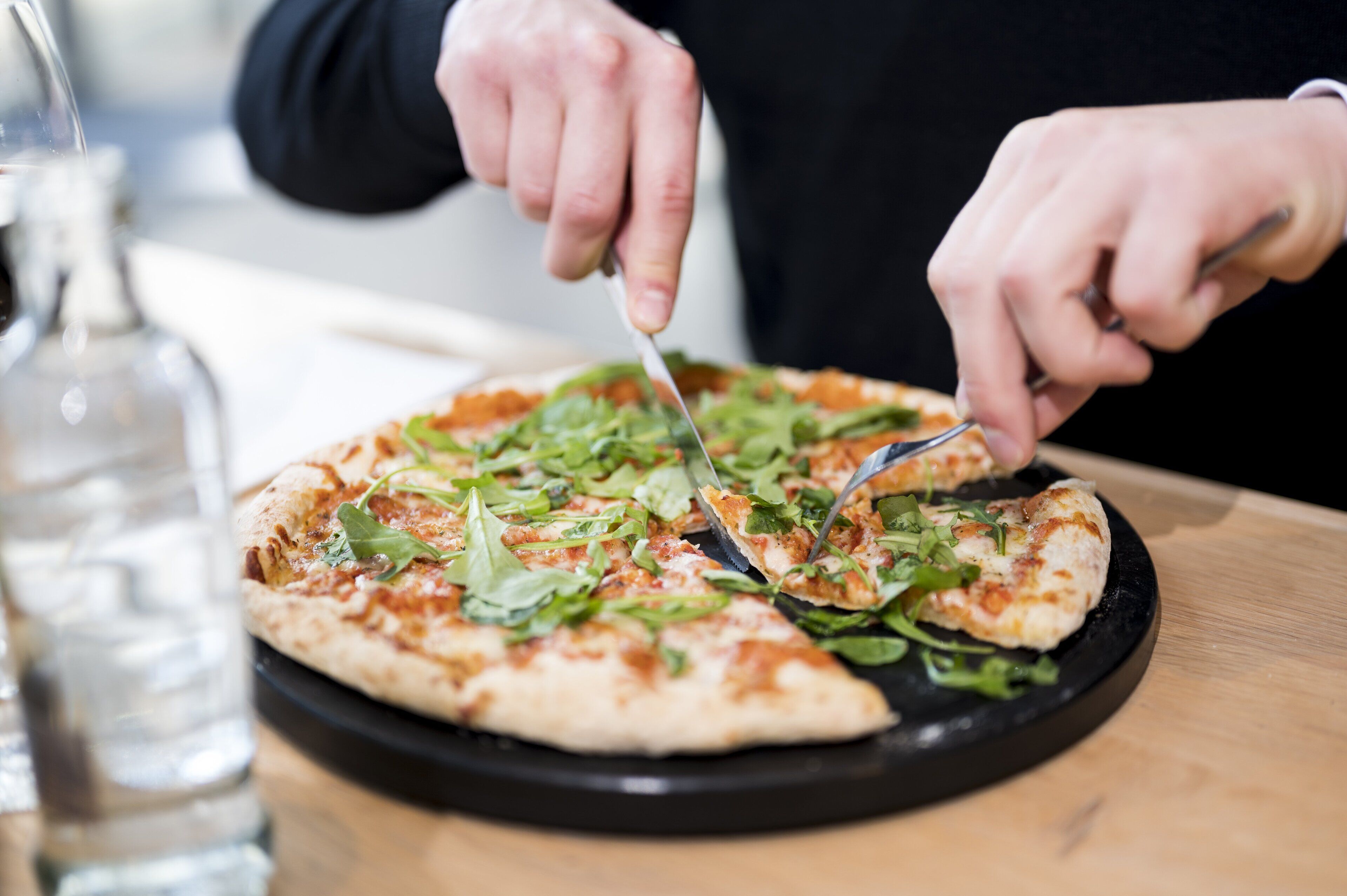 Una persona cortando una pizza en un plato negro.