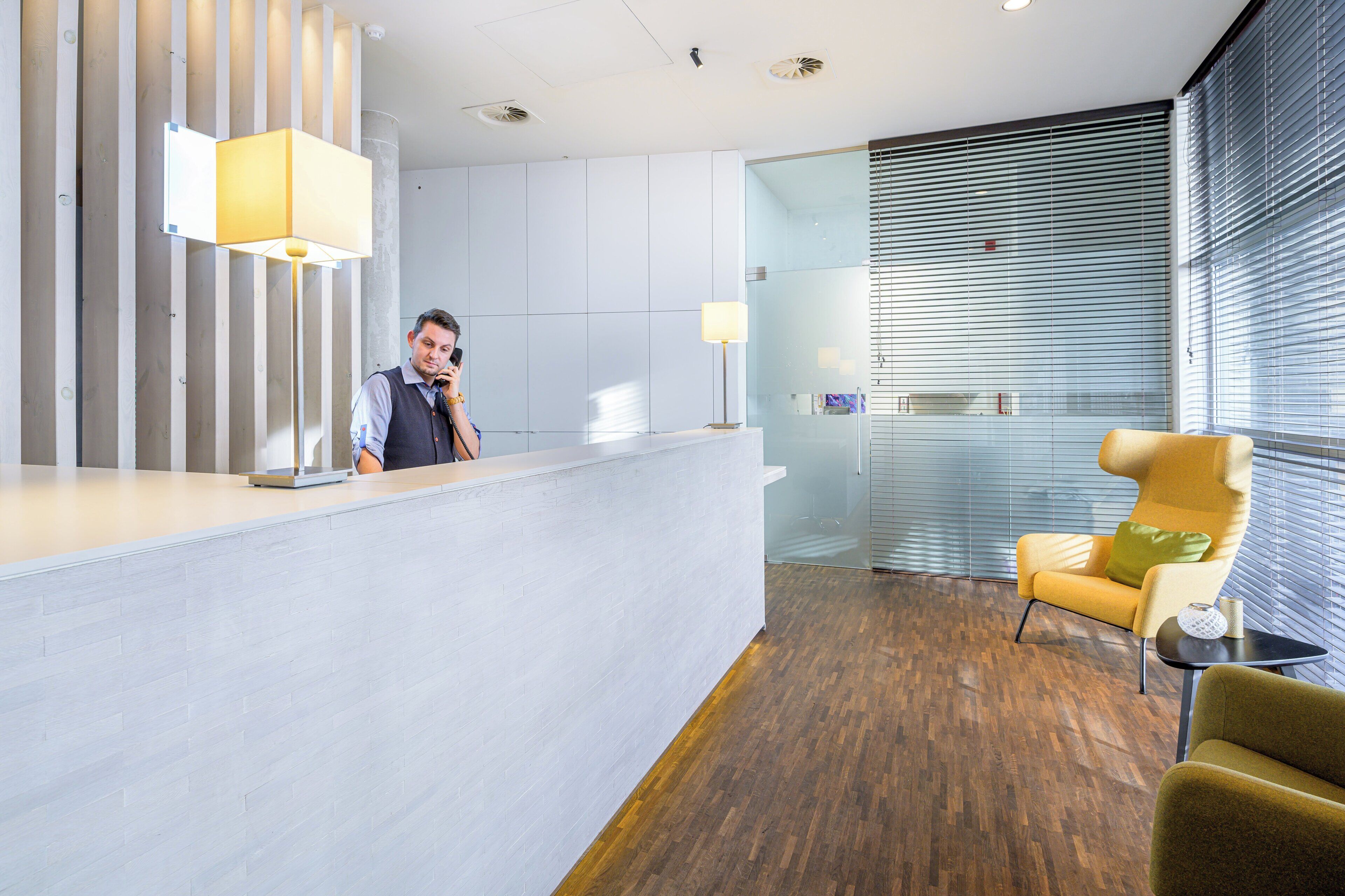 A modern reception area with a reception desk, a standing lamp, a glass partition, and a yellow armchair.