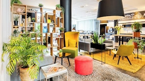 Un área de estar moderna con un sillón amarillo, un reposapiés rojo y diversas plantas.