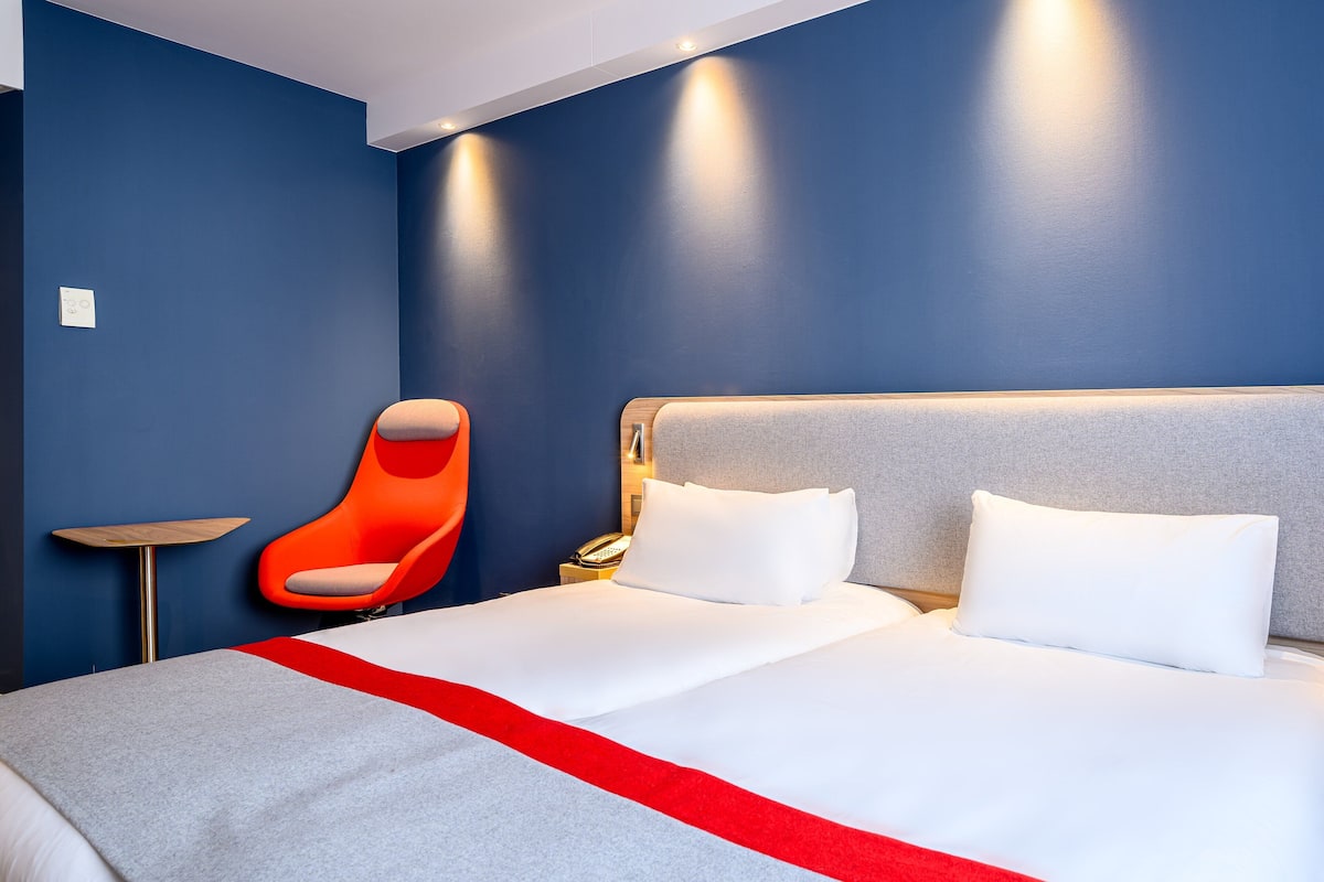 A hotel room with a large bed, a red chair, and a small table.