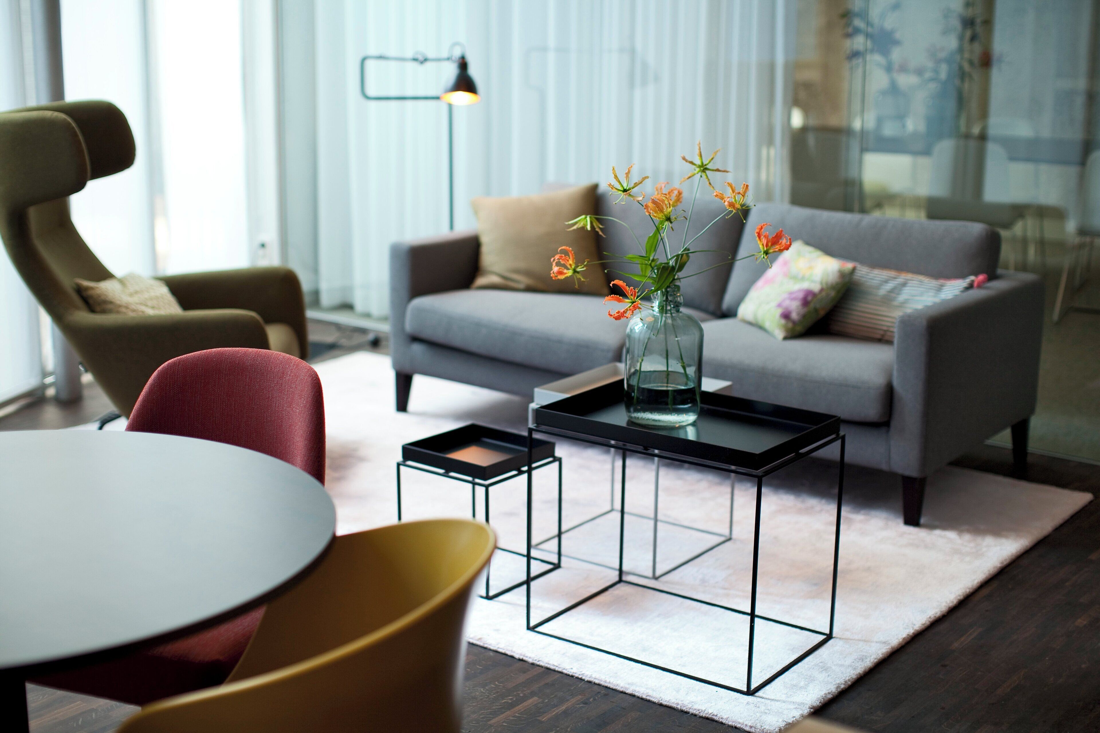 A modern living room with a grey sofa, a red chair, a glass coffee table, and a vase with flowers.