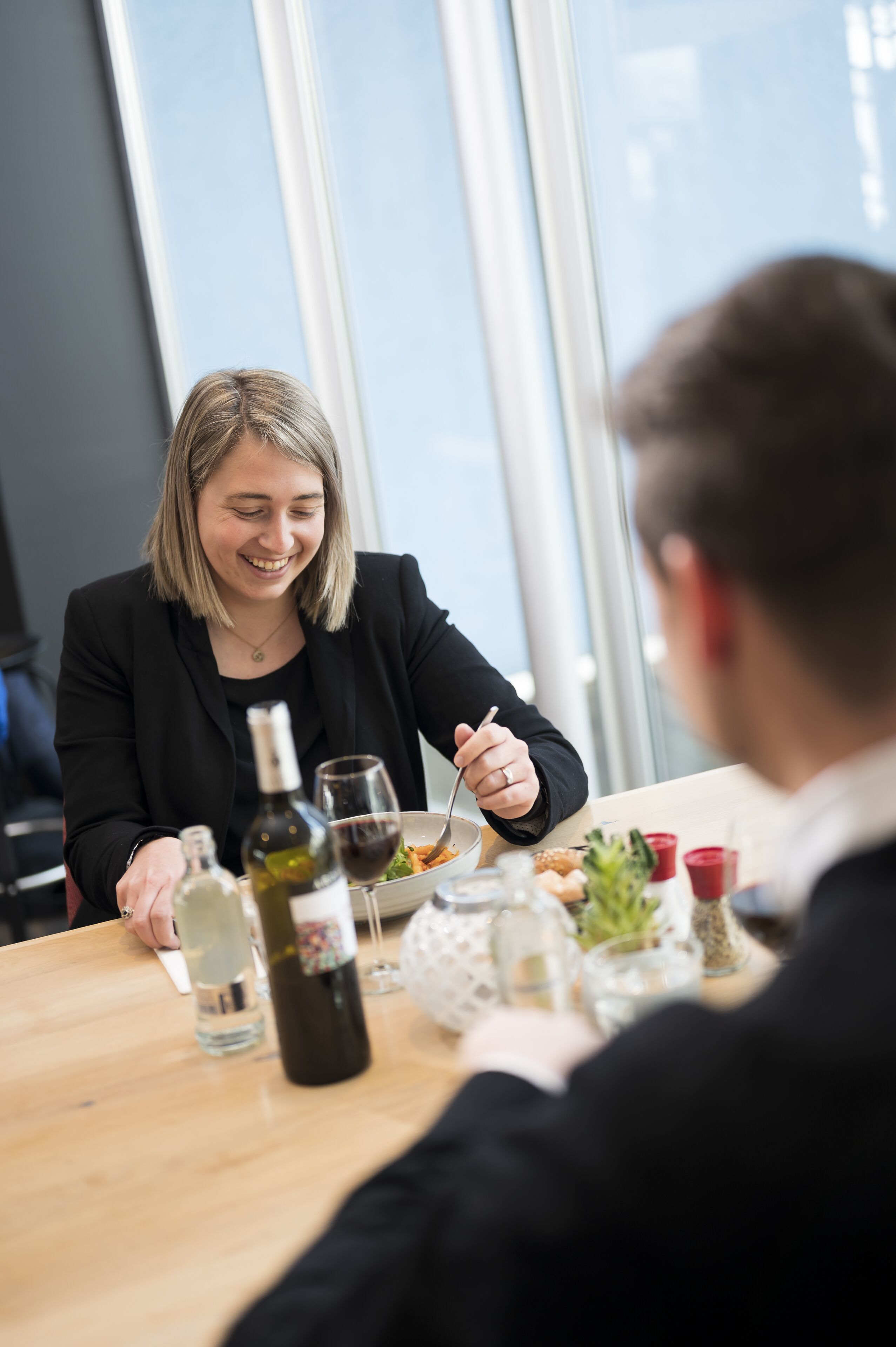 Iemand zit aan een tafel met een fles wijn, een glas en een bord eten.