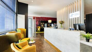 Een modern ingerichte receptiezone, met een receptiebalie, zithoek met fauteuils en een goed zichtbaar Holiday Inn Express bord.
