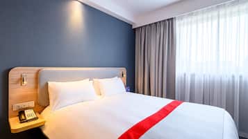 A hotel room with a large bed, a bedside table with a telephone, and a window with curtains.