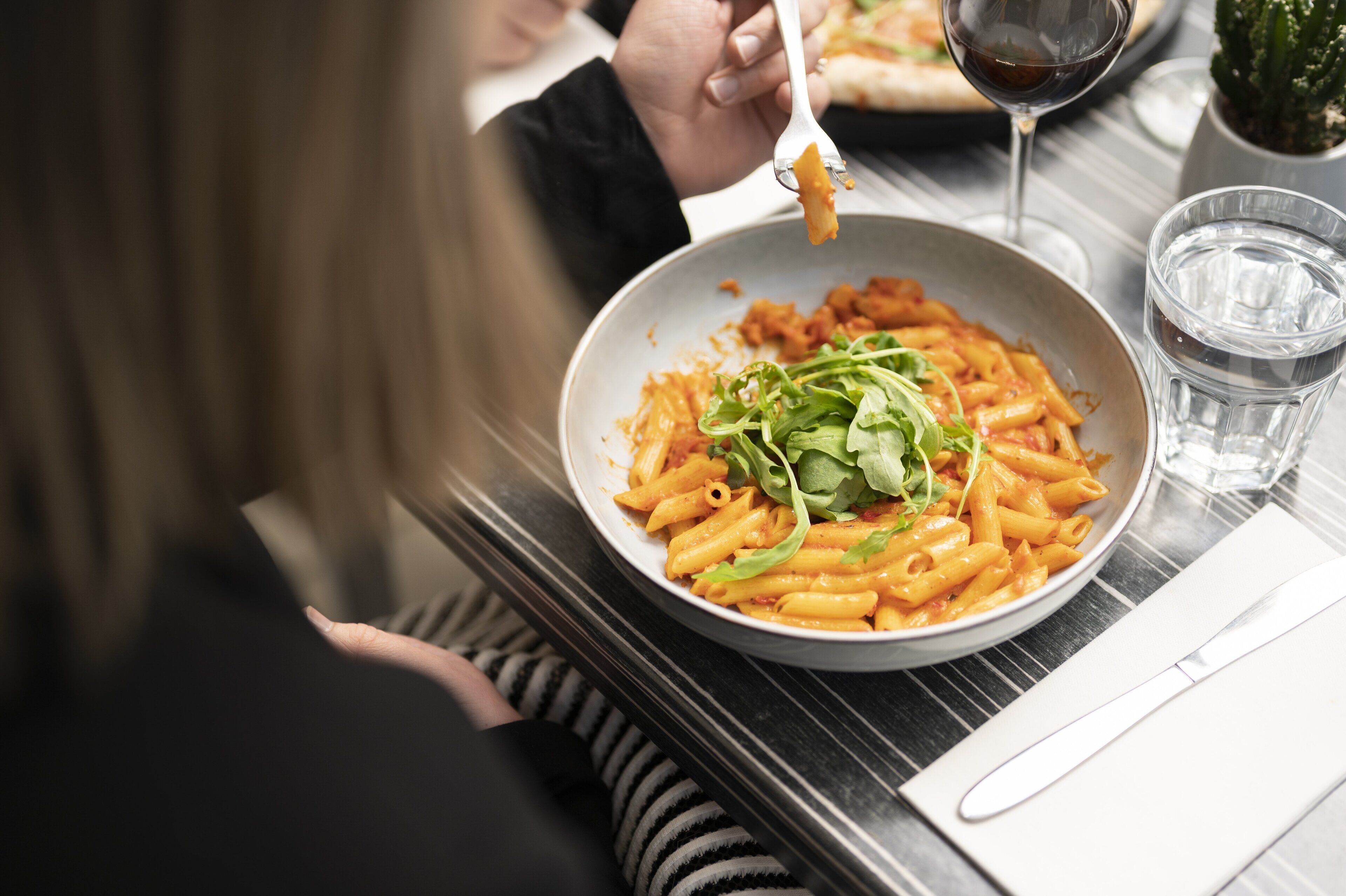 A dining table with a plate of pasta, a glass of water, and a wine glass.