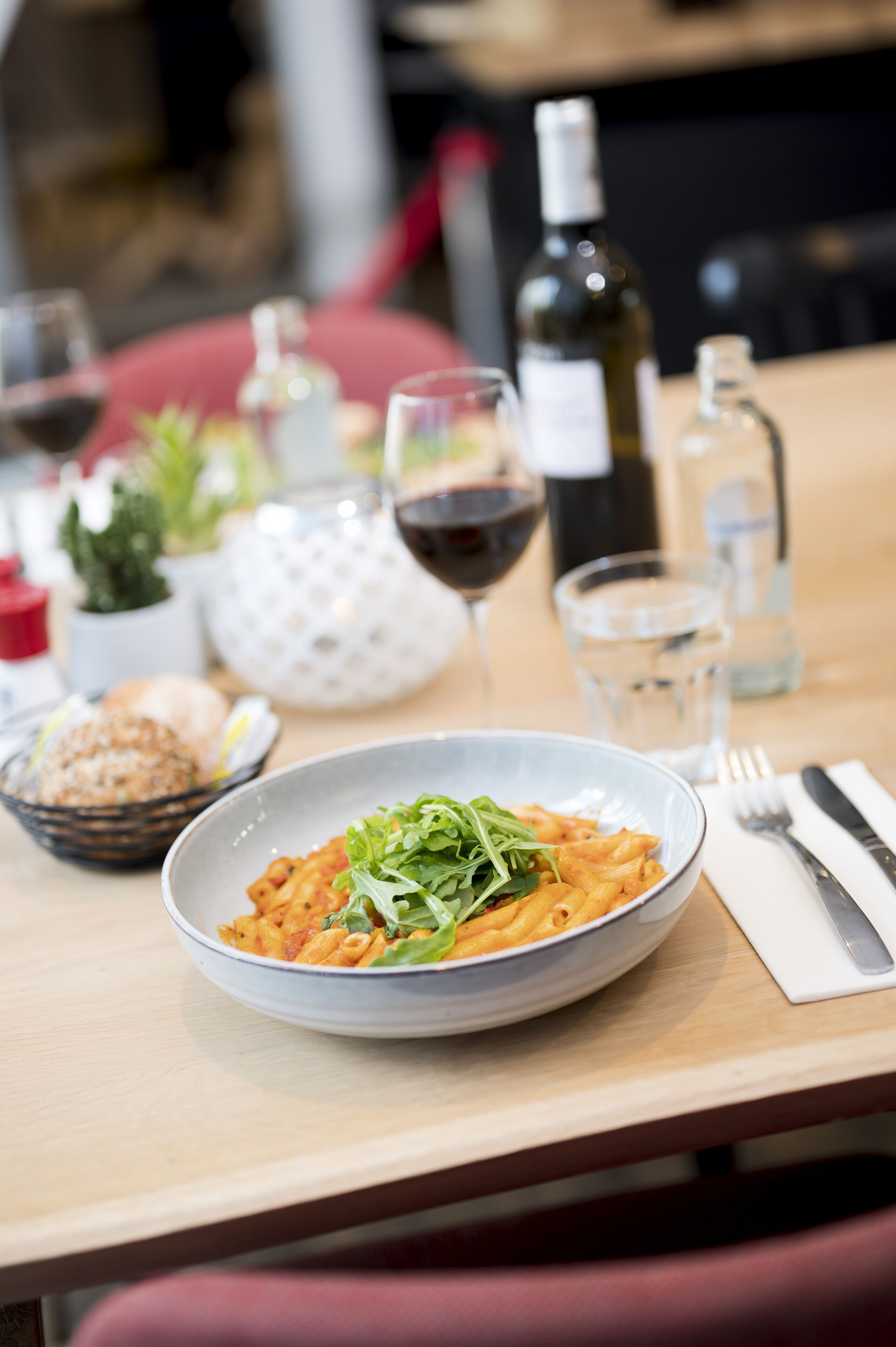 A dining table with a plate of pasta, a wine glass, and a bottle of wine.