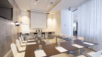 A conference room with a long table, white chairs, and a projector screen.