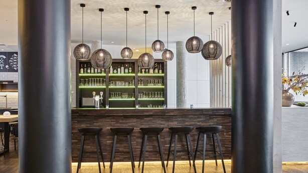 Zona de bar con taburetes de madera, una barra y lámparas colgantes de mimbre.