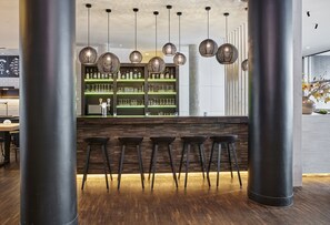 A bar area with wooden stools, a bar counter, and hanging wicker light fixtures.