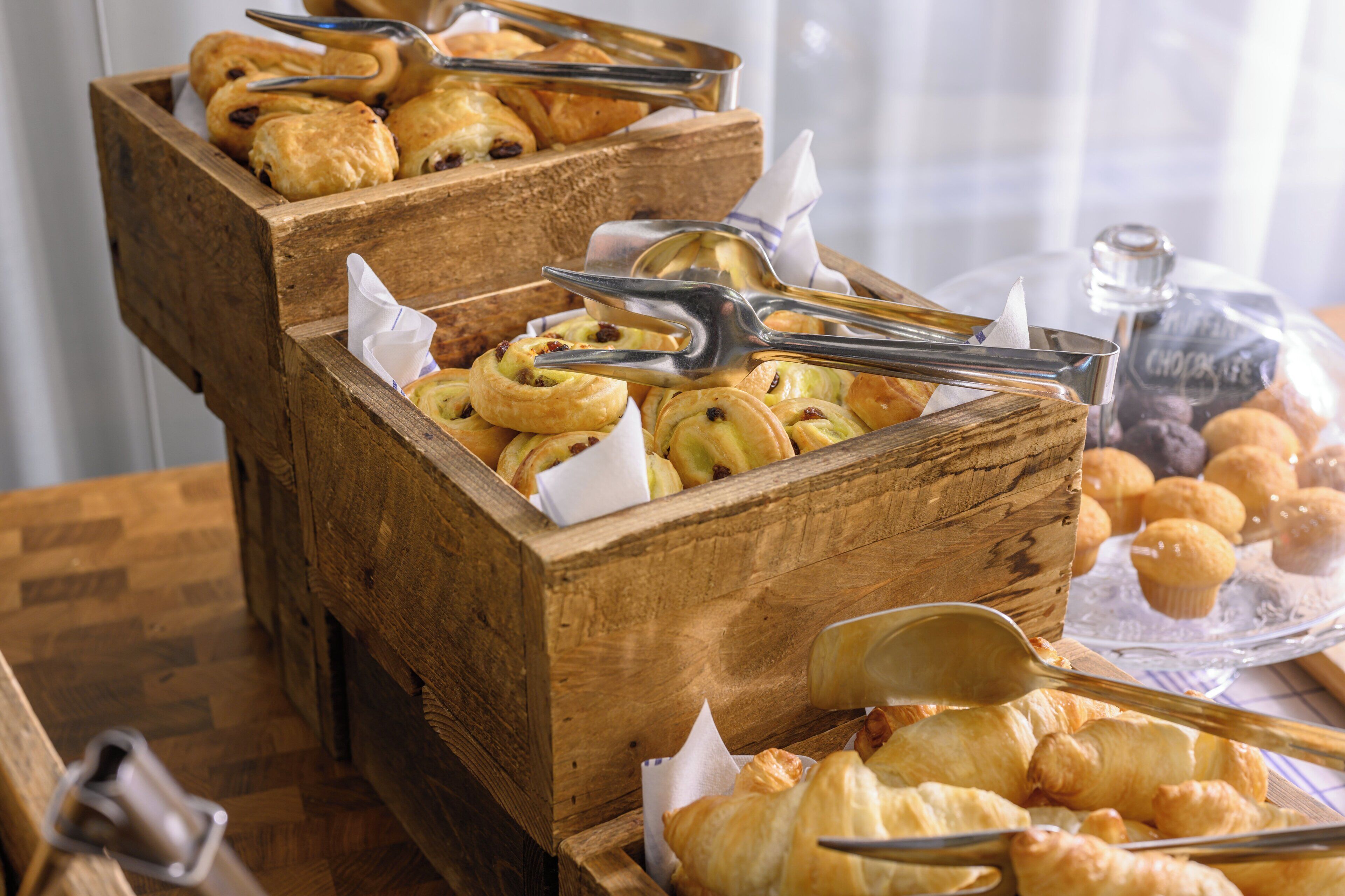 A wooden buffet table with various baked goods, including pastries and muffins, arranged in wooden boxes.