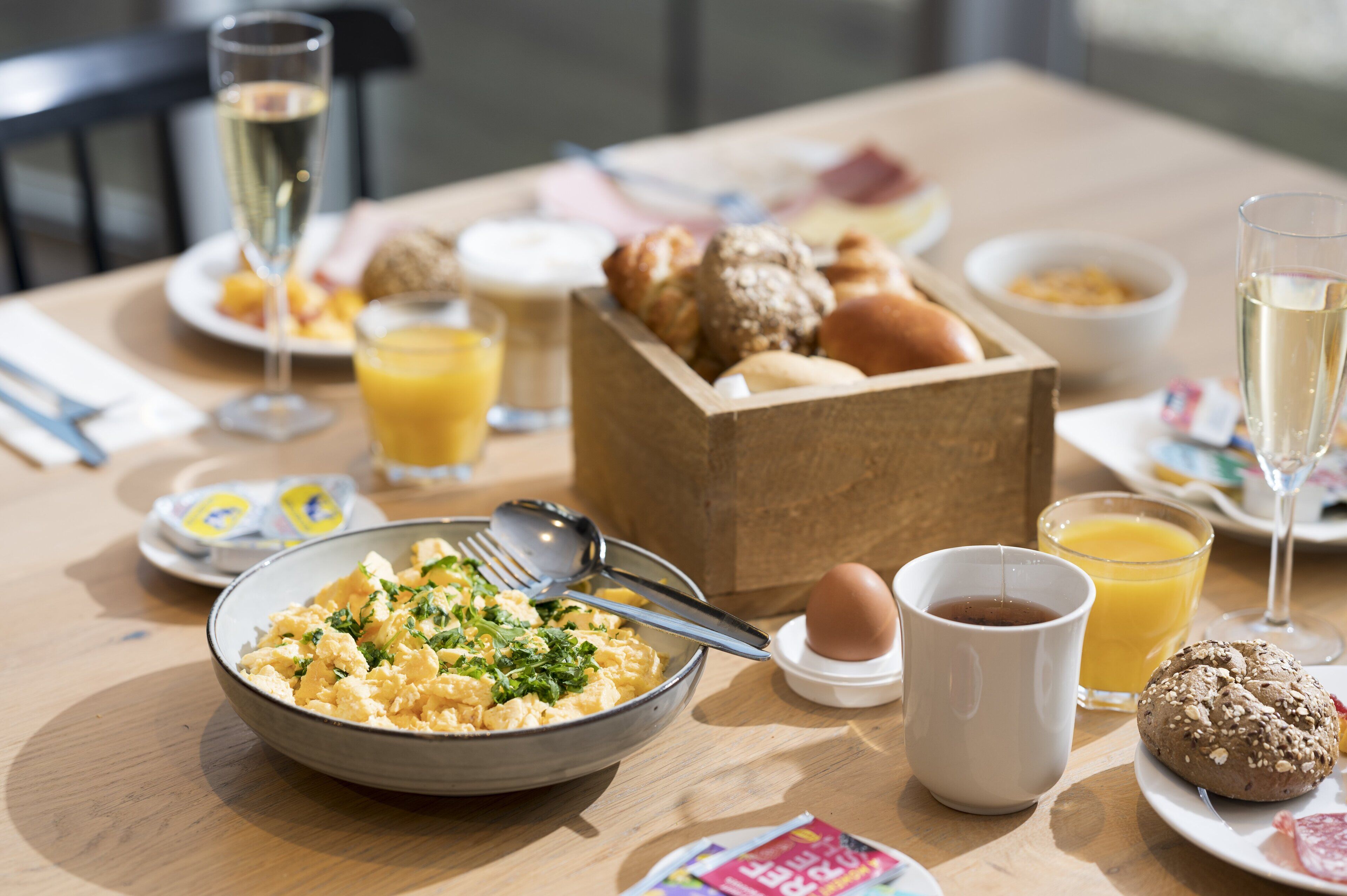 A breakfast table with scrambled eggs, toast, a muffin, a glass of orange juice, a cup of coffee, and a glass of champagne.