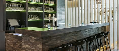 A modern bar area with a wooden counter, multiple shelves of bottles, and a selection of glasses.