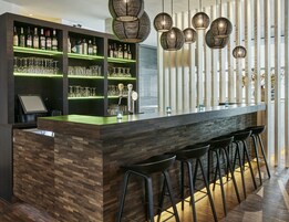 Zona de bar moderna con una barra de madera, varias estanterías llenas de botellas y una selección de vasos.